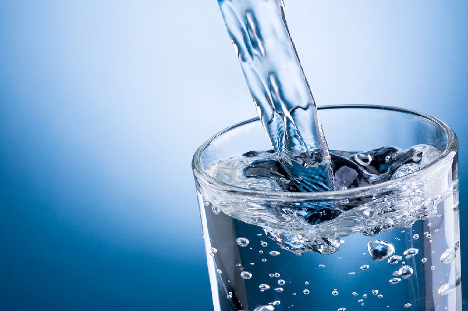 Water is being poured into a glass on a blue background.
