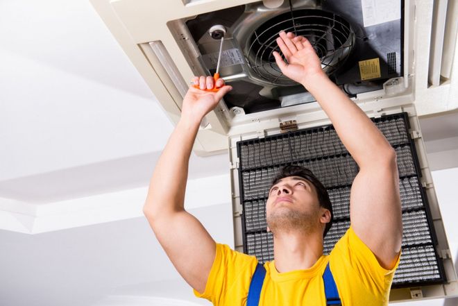 A man is fixing an air conditioner with a screwdriver.