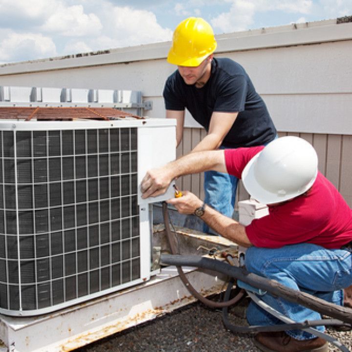 Two men wearing hard hats are working on an air conditioner