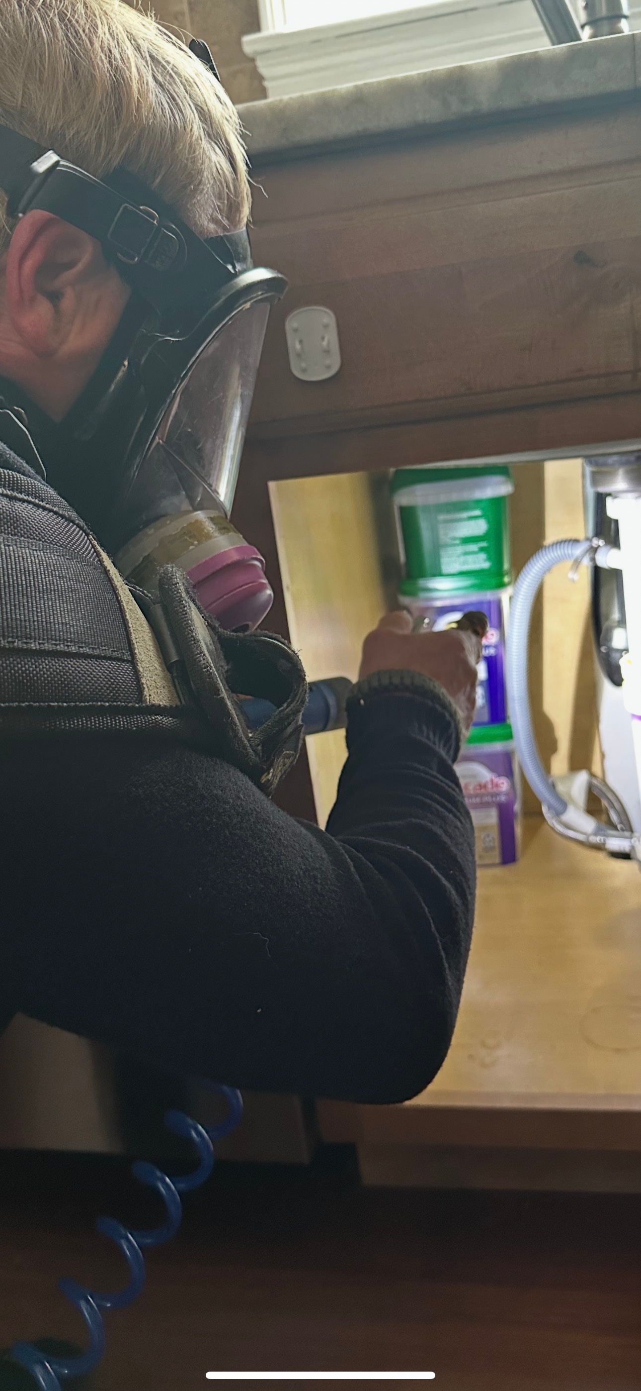 A man wearing a gas mask is working on a kitchen sink.