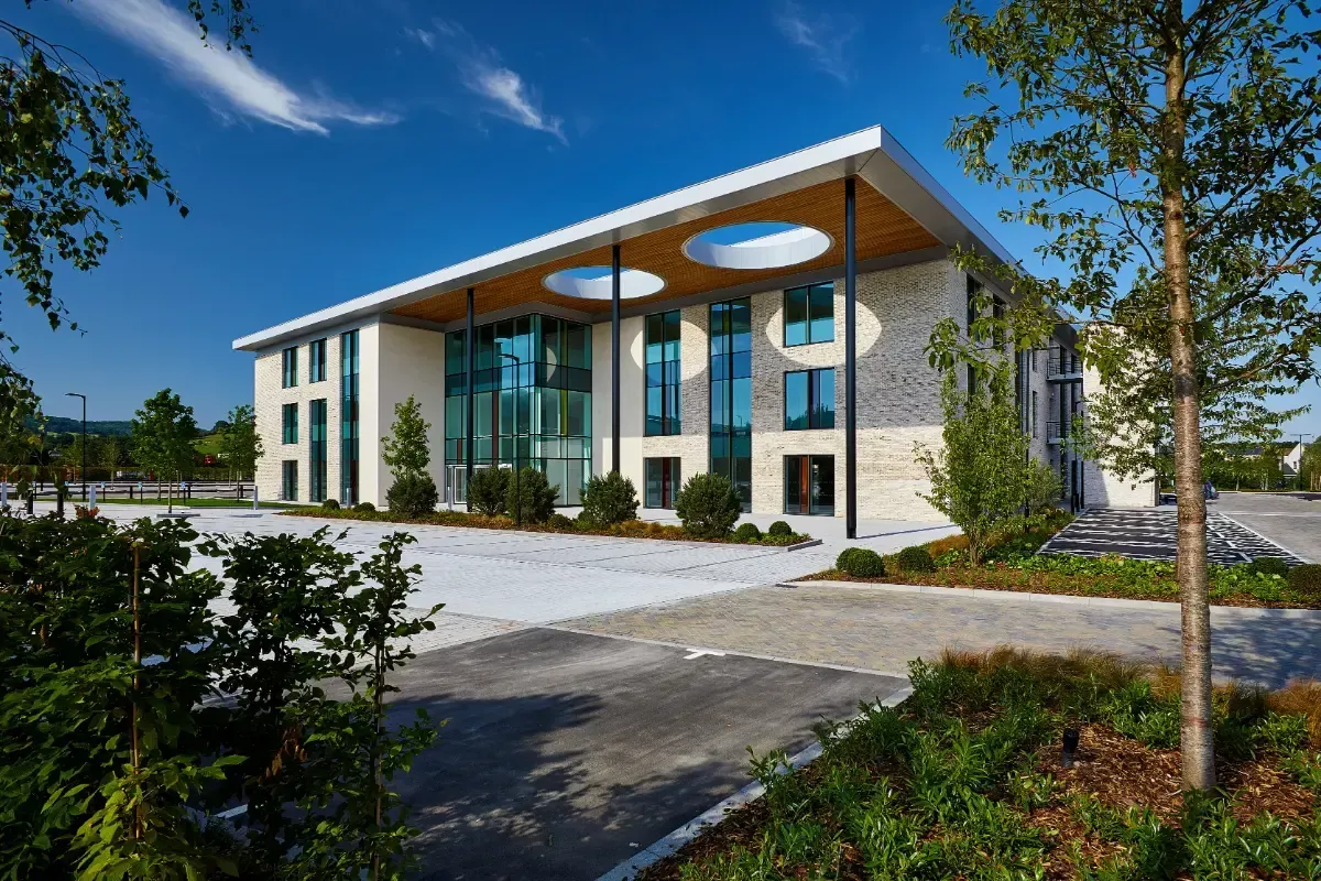 Modern two-story building with glass entrance and stone columns on a landscaped campus under a blue sky