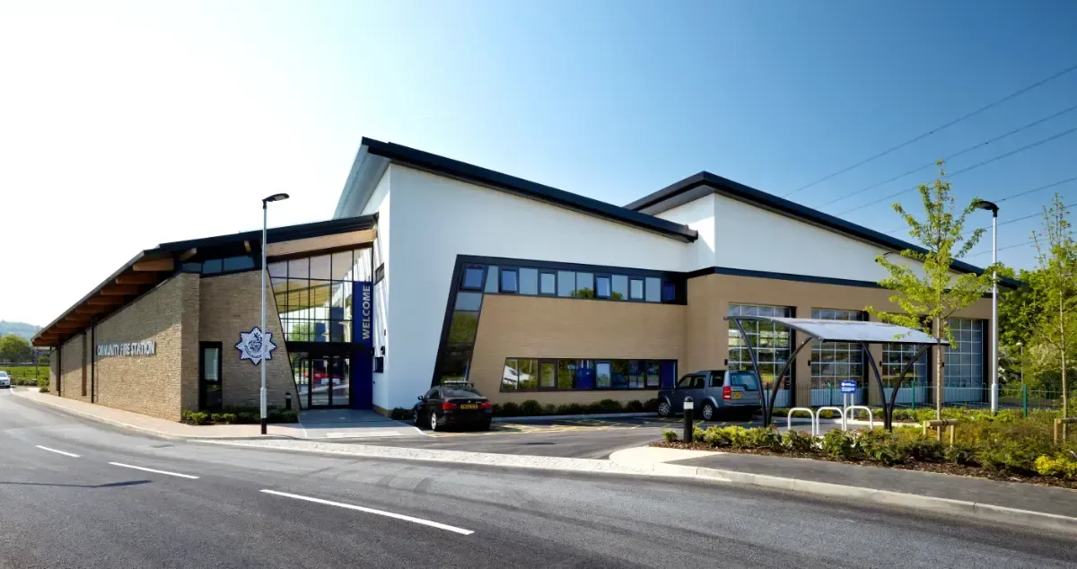 Modern building exterior with a curved entrance, large windows, and a parking lot under a blue sky
