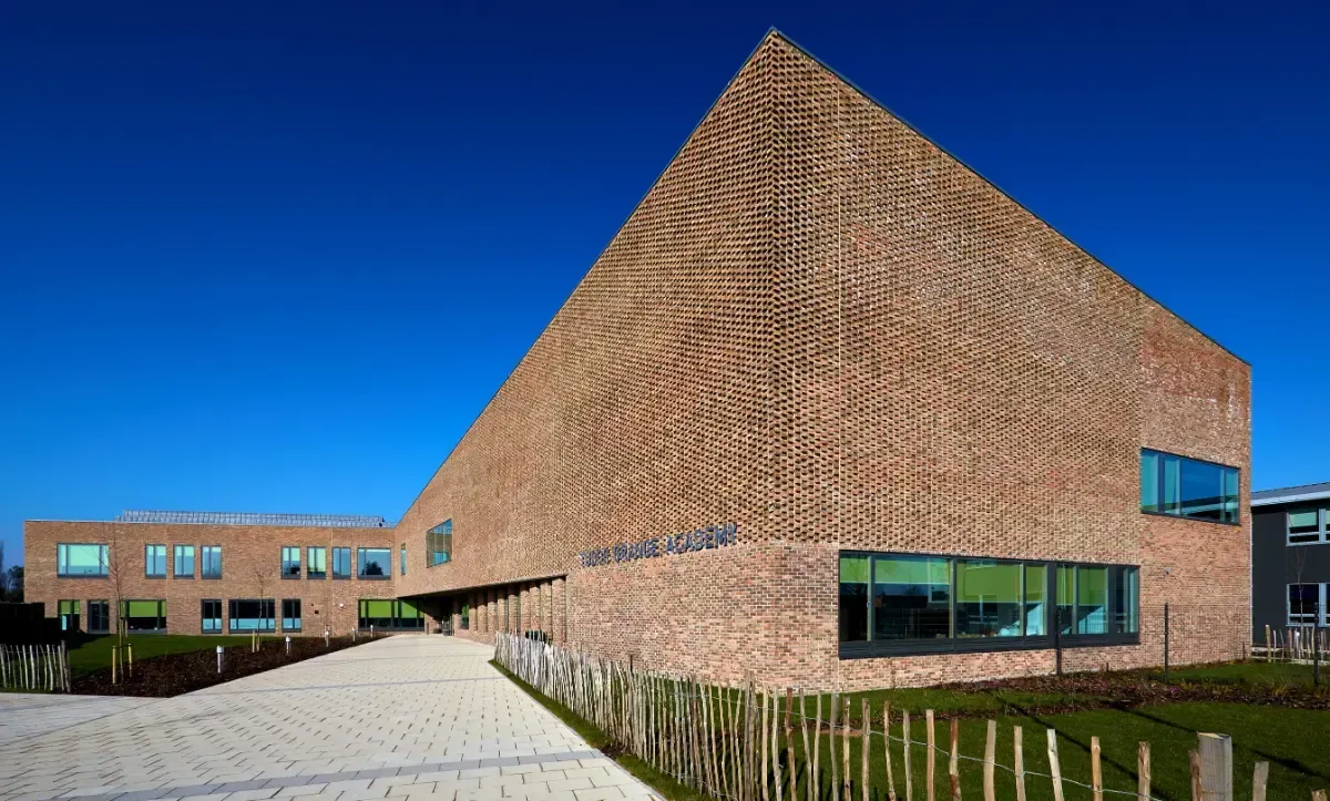 Modern brick building with a sloped facade, blue windows, and a paved courtyard under a clear blue sky