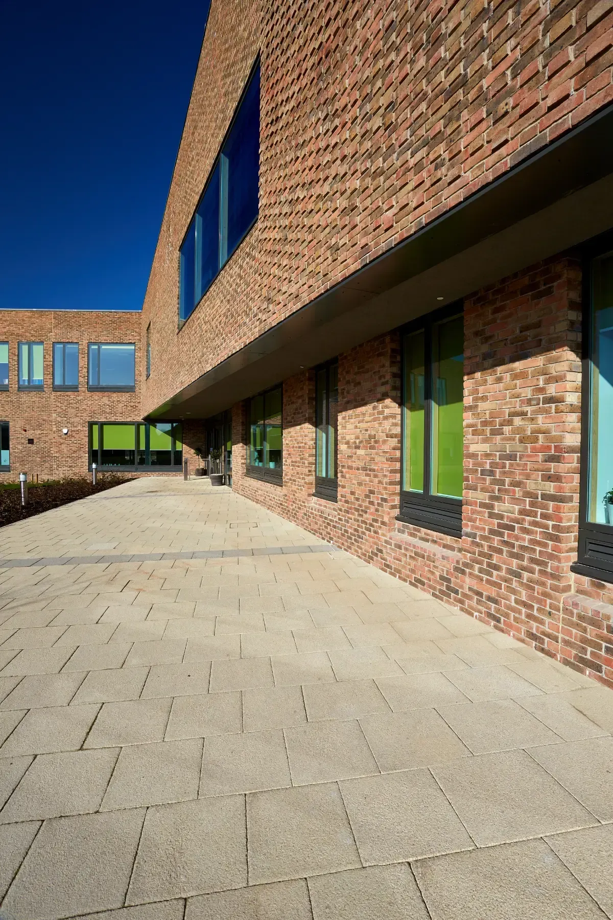 Brick building walkway with green windows under a clear blue sky