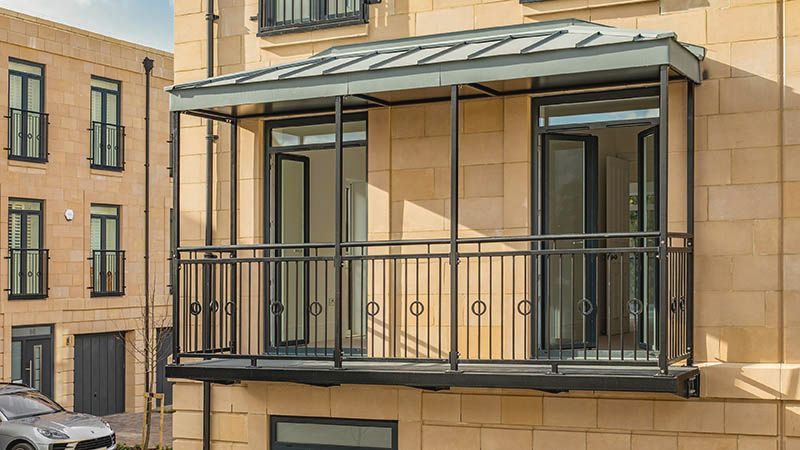 Modern apartment balcony with black metal railing and glass awning on a tan building