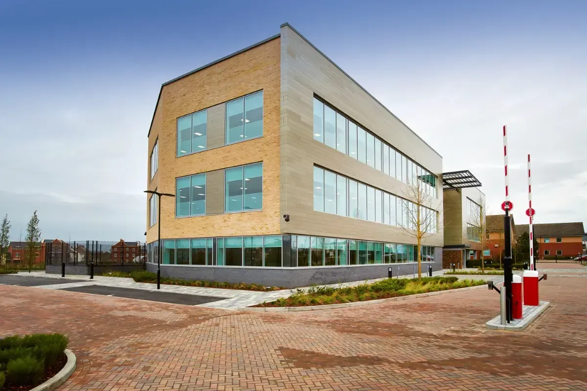 Modern tan office building with large windows, brick courtyard, and red-and-white poles outside