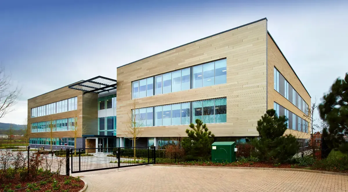 Modern three-story office building with tan brick, blue windows, and a landscaped entrance