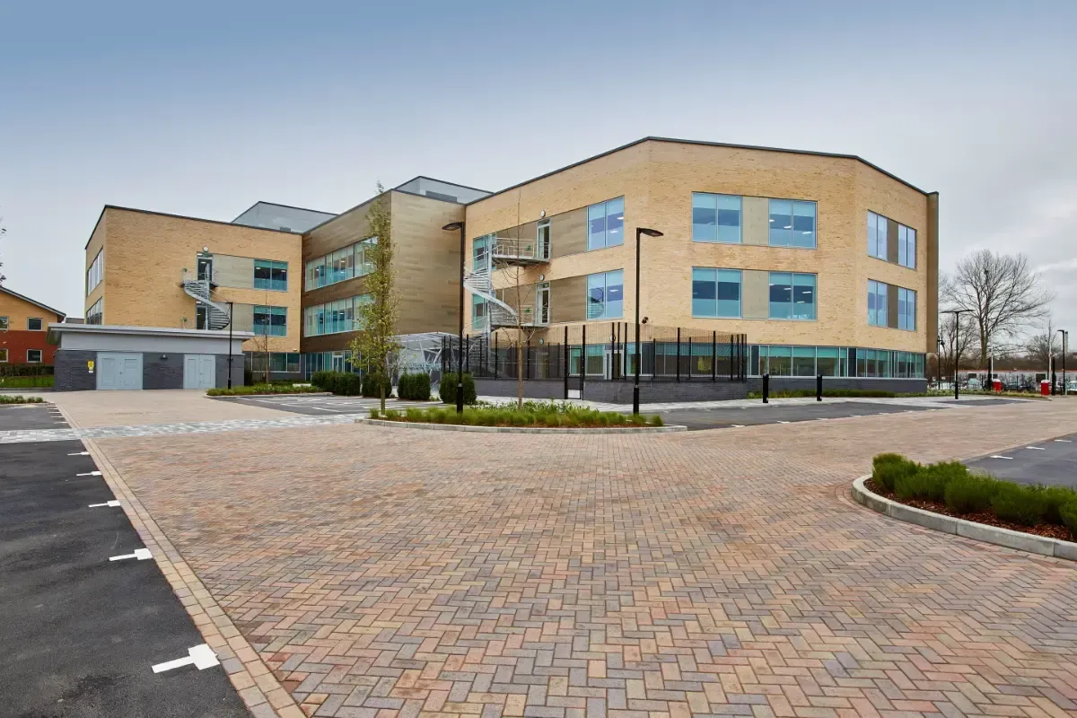 Modern brick office building with large windows and a paved parking lot under an overcast sky