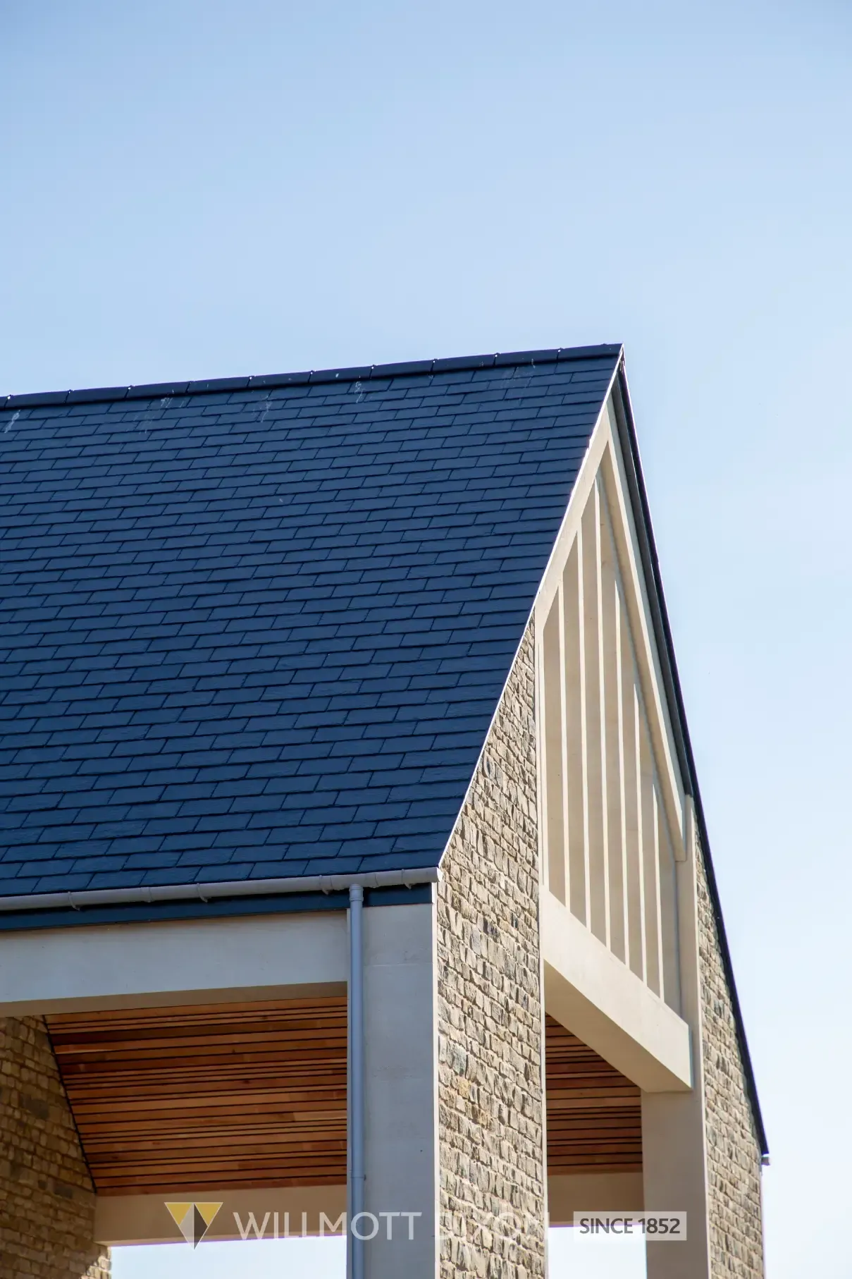 Blue shingled house roof and stone exterior corner against a clear sky