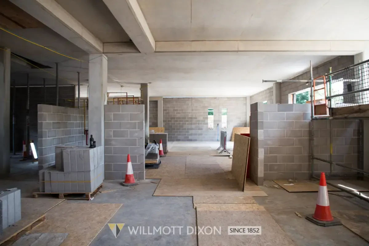Indoor construction site with cinder block walls, traffic cones, and scaffolding under a concrete ceiling