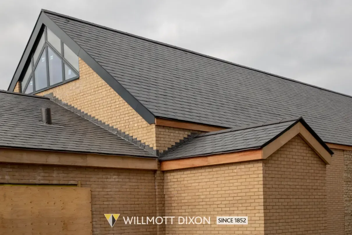 Modern brick house roof with dark gray shingles and a dormer window under a cloudy sky