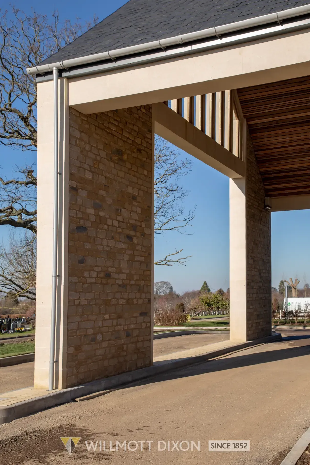 Modern building entrance with stone columns, cream trim, and a covered walkway overlooking a park.