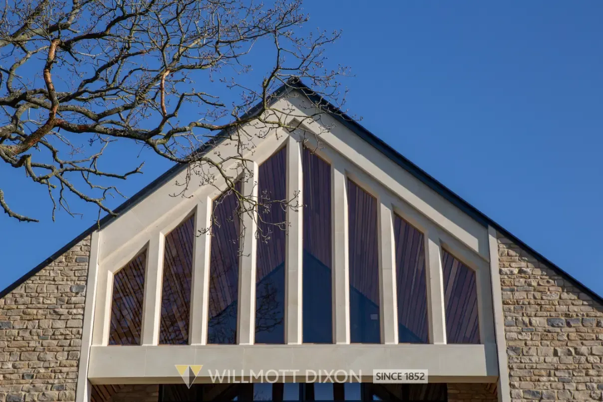 Stone building facade with triangular glass window panels under a blue sky and bare tree branches