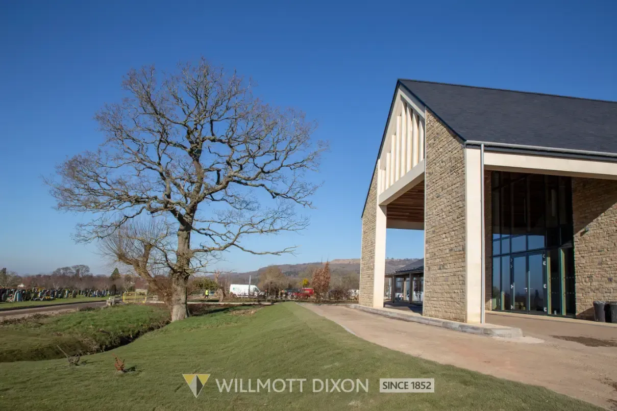 Modern house with large windows beside a leafless tree on a sunny rural lawn
