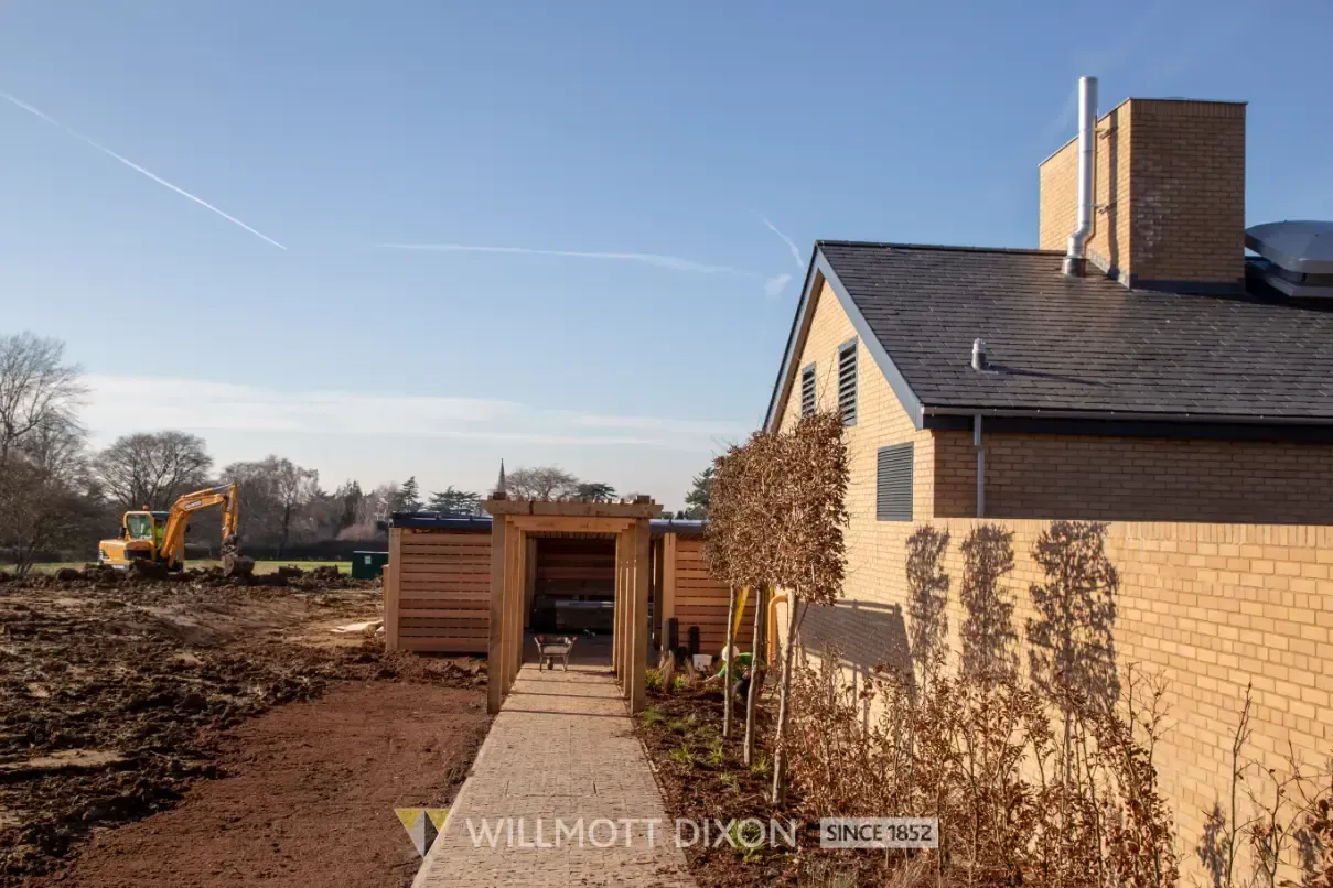 Backyard with wooden deck and house beside a muddy construction site under a clear blue sky