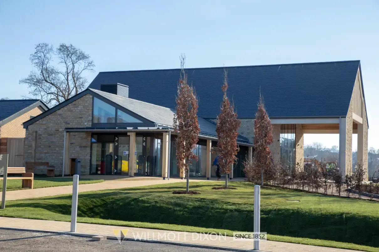 Modern brick building with glass entrance, dark roof, and landscaped lawn on a sunny day