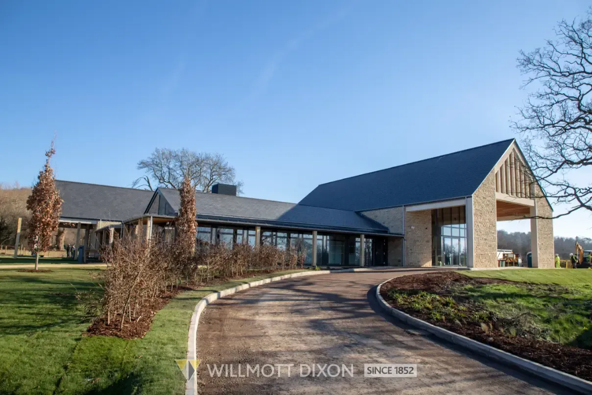 Modern building with a dark roof, glass entry, and curved driveway under a clear blue sky.
