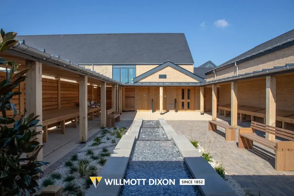 Open-air courtyard with timber colonnades and a central gravel path under a blue sky