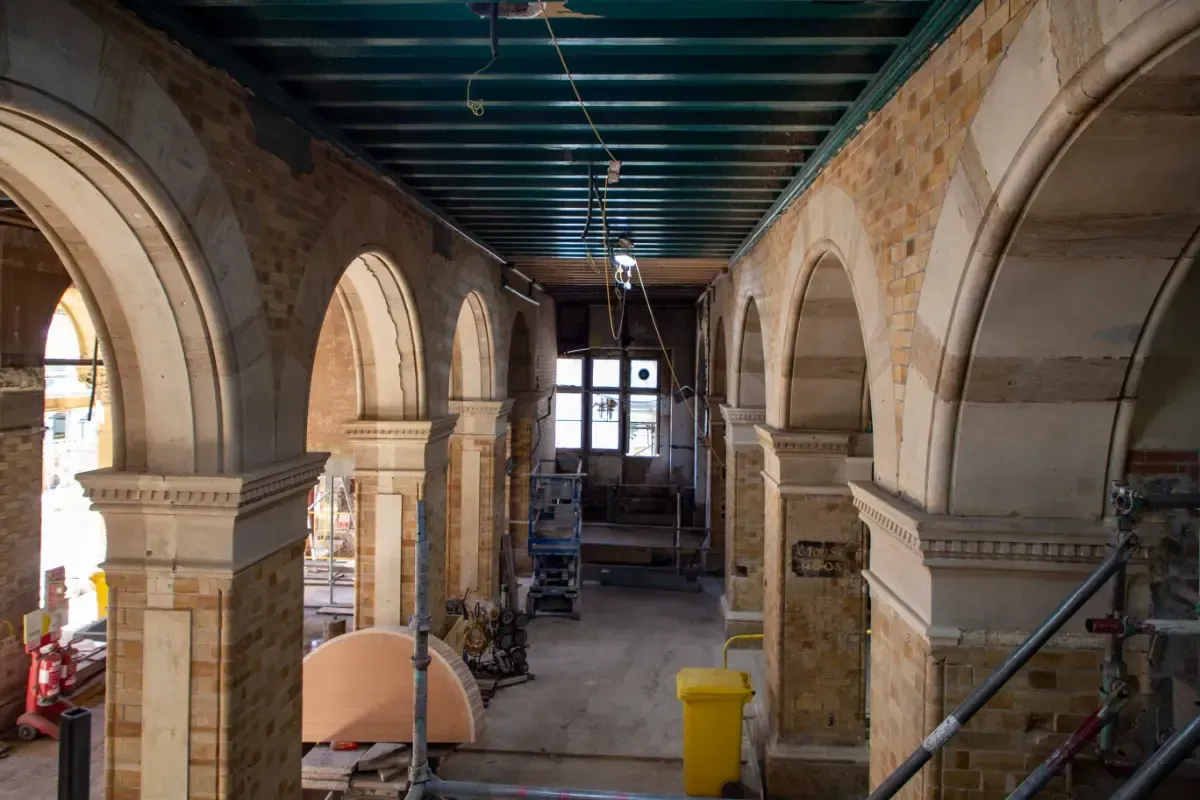 Interior of a stone building under renovation, with arched openings, scaffolding, and tools inside.