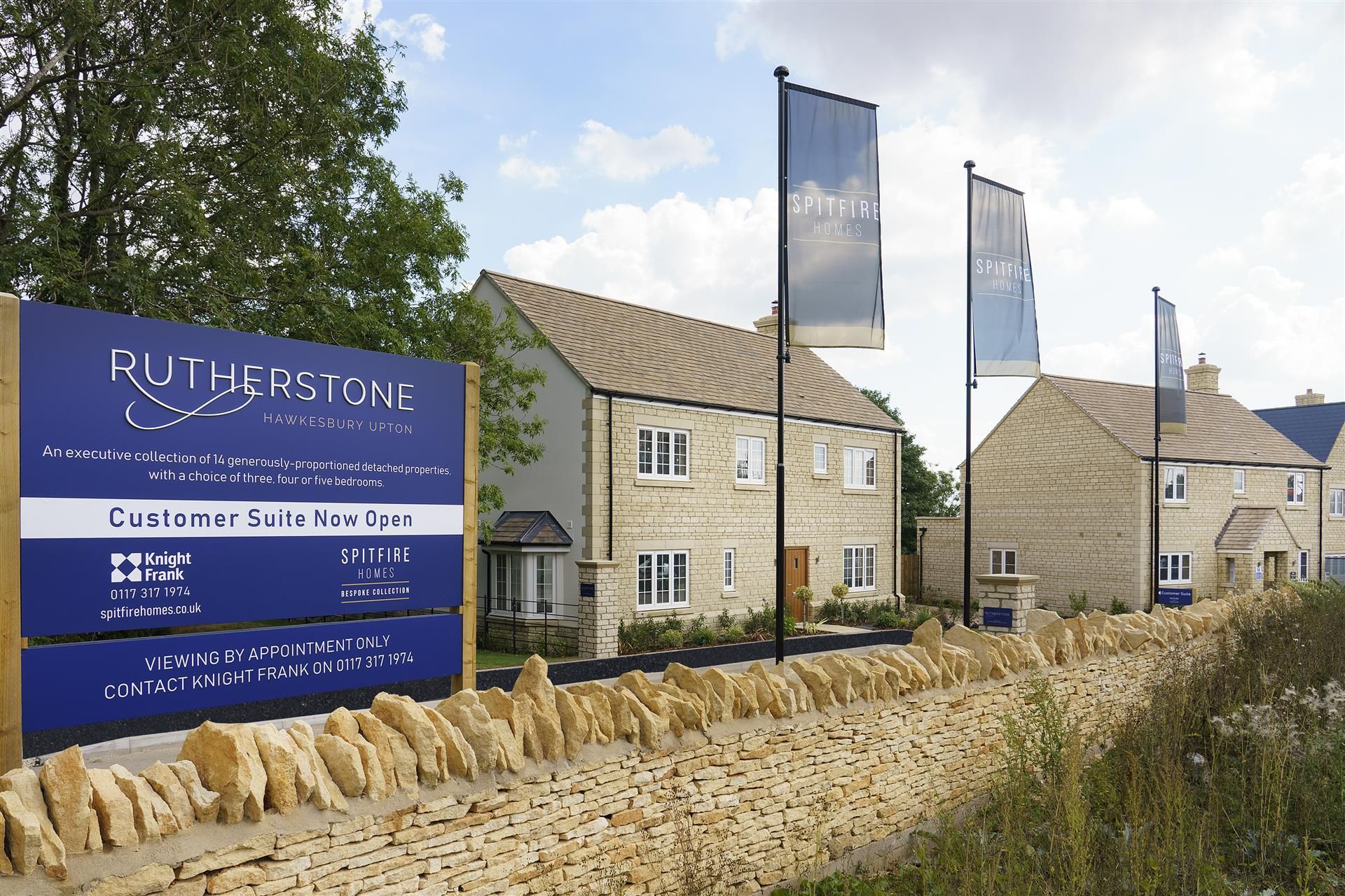 Blue sign outside a stone hotel and cottages with flags along a rural roadside under a cloudy sky