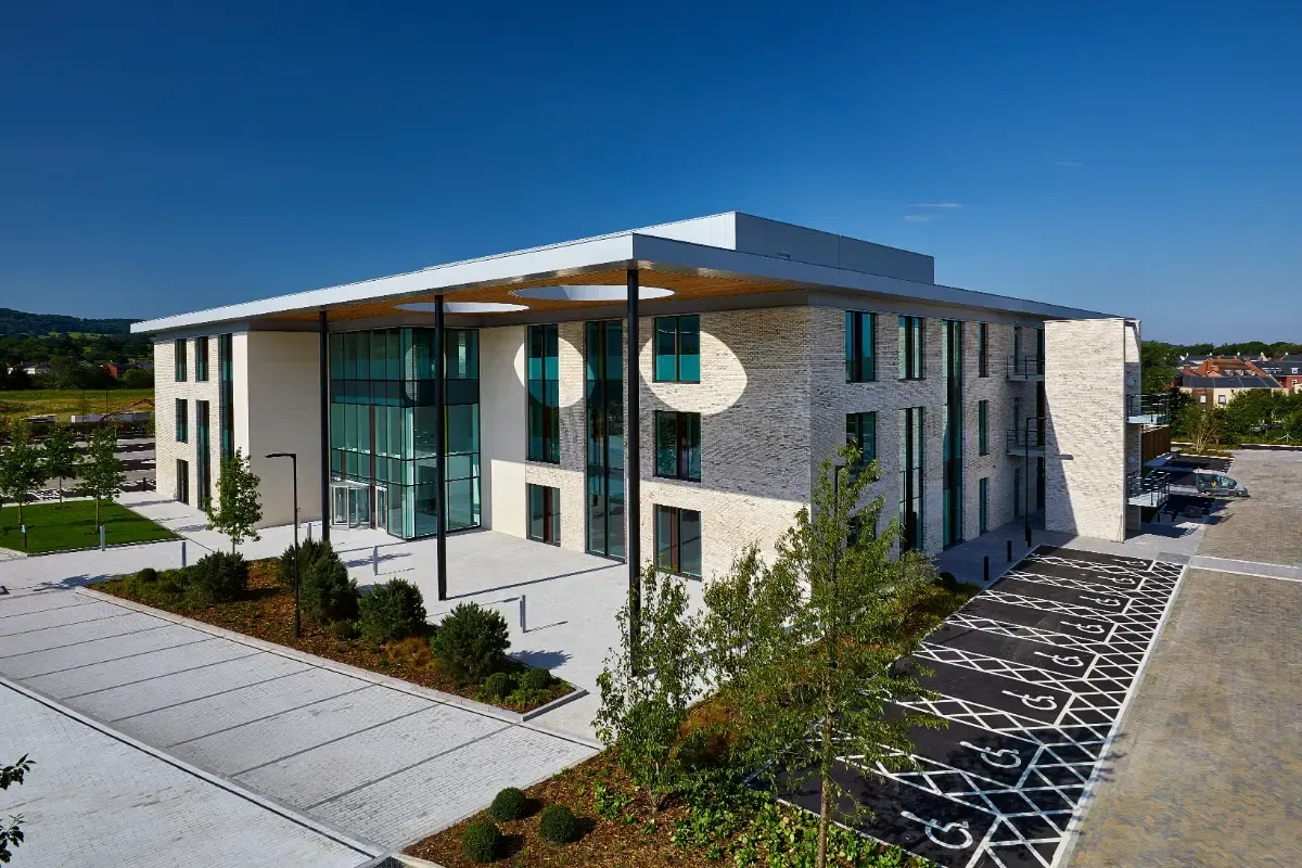 Modern office building with glass entrance, white exterior, and parking lot under clear blue sky