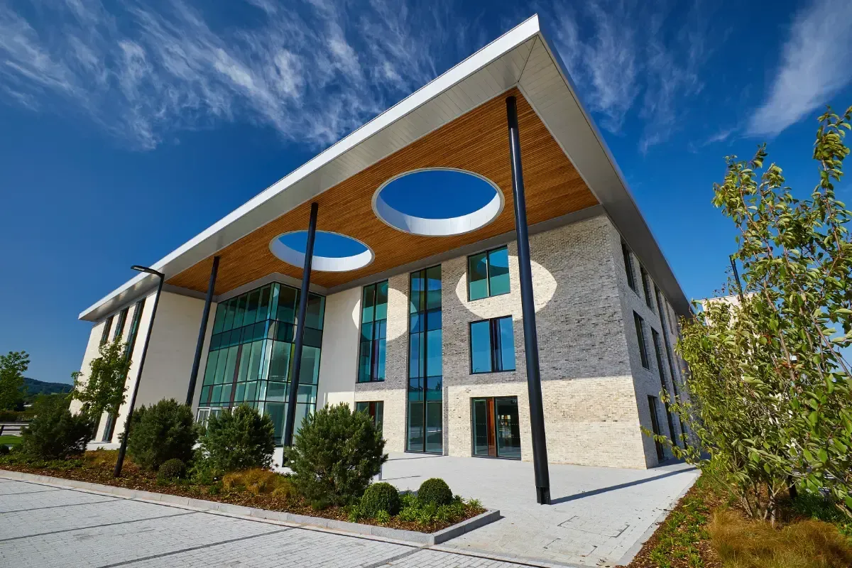 Modern building with a slanted roof, blue circular skylights, and large windows under a clear sky