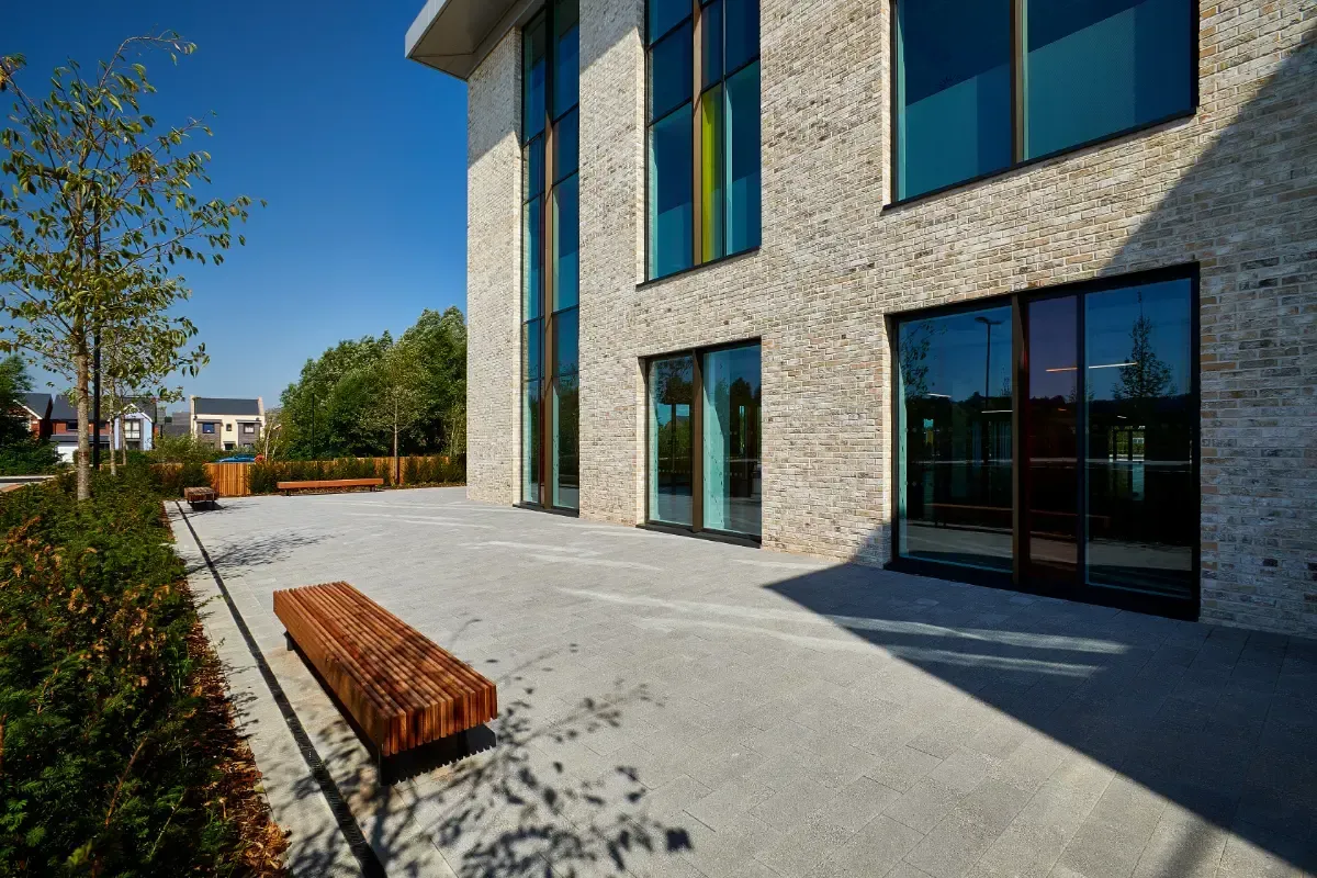 Modern brick building courtyard with wooden bench, paved patio, and glass windows in sunlight