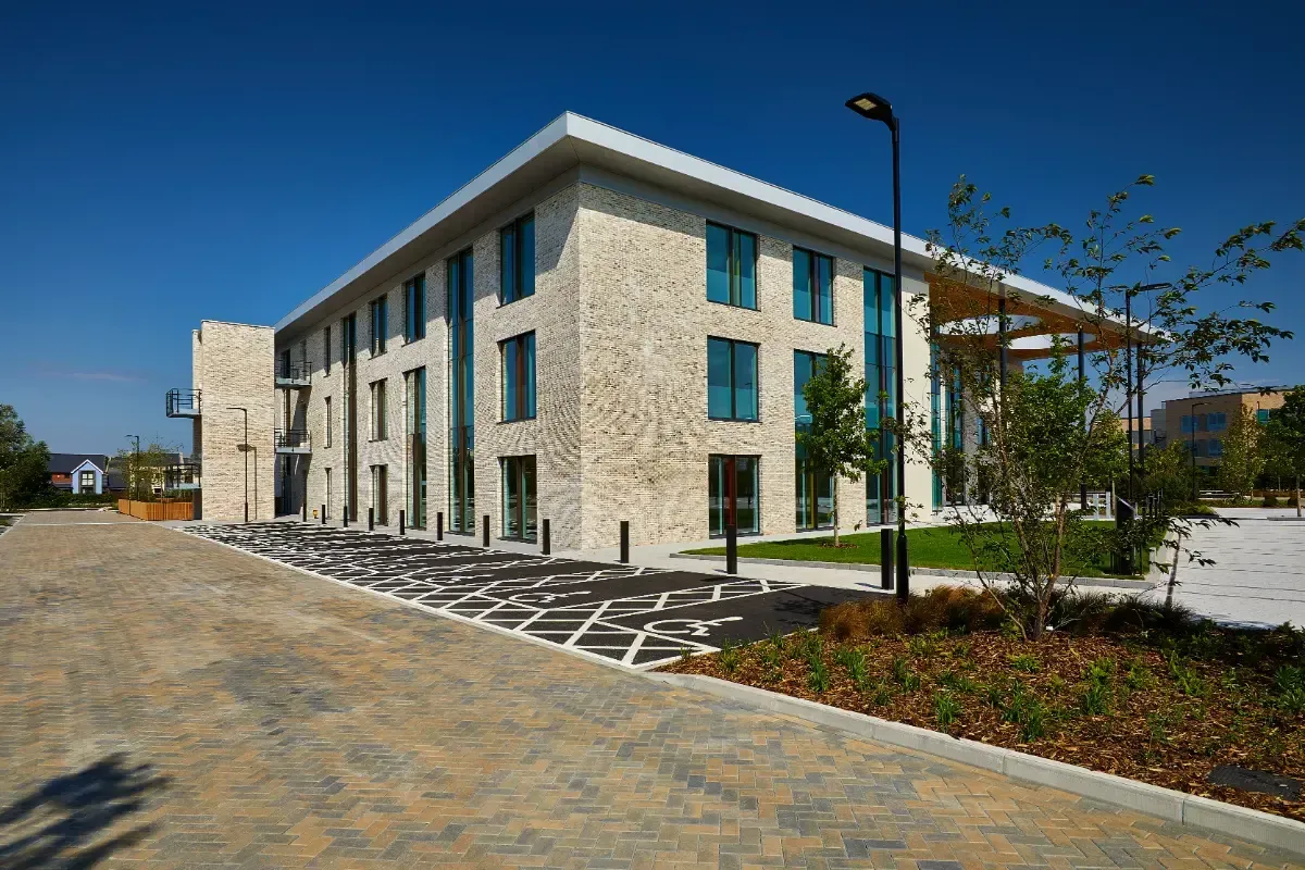 Modern two-story stone building with blue windows beside a paved walkway and landscaped grounds