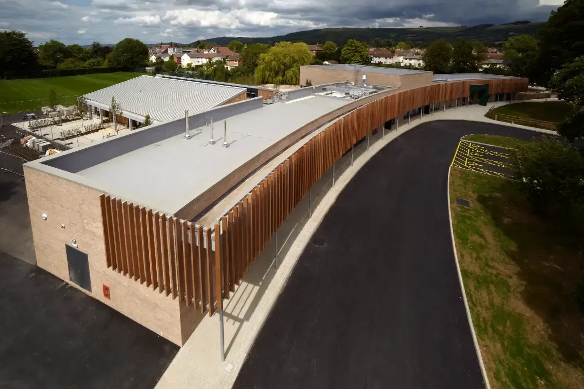 Aerial view of a modern curved building with wood slats beside a paved road and trees