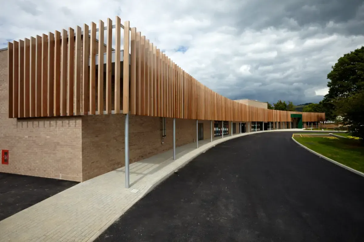 Modern building with wooden slatted facade beside a curved driveway under a cloudy sky