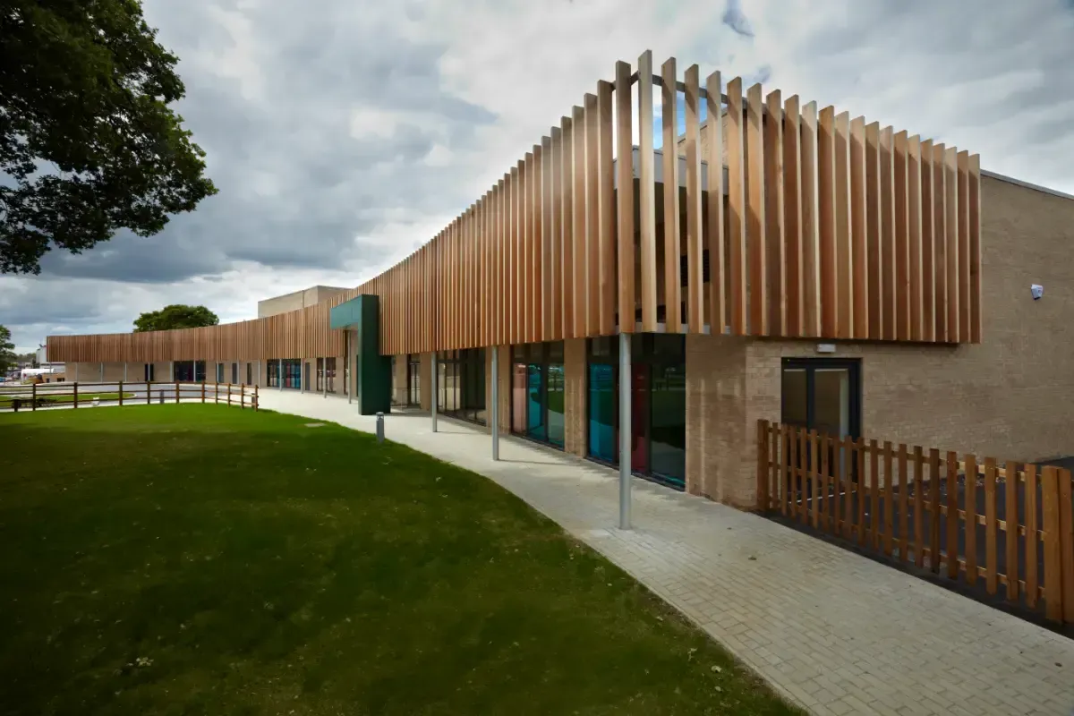 Modern wooden building with vertical slats, curved walkway, and green lawn under cloudy sky