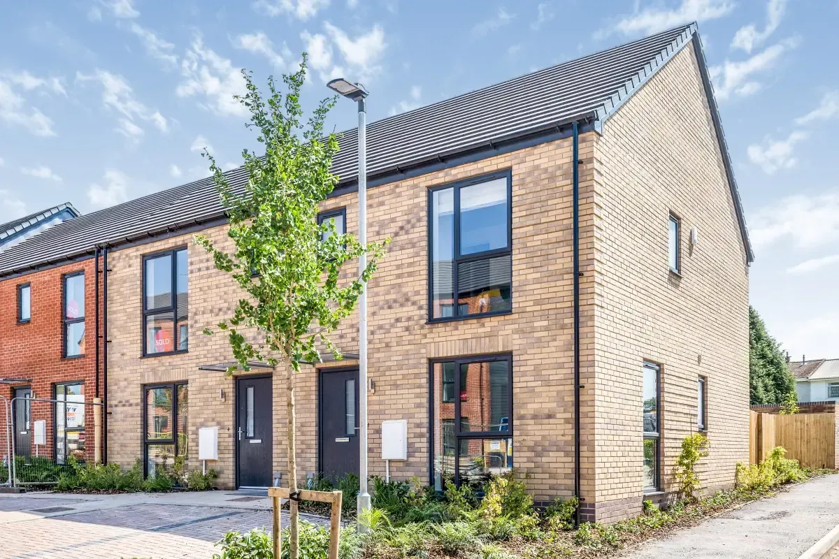 Row of modern brick townhouses with black roofs and front gardens on a sunny day