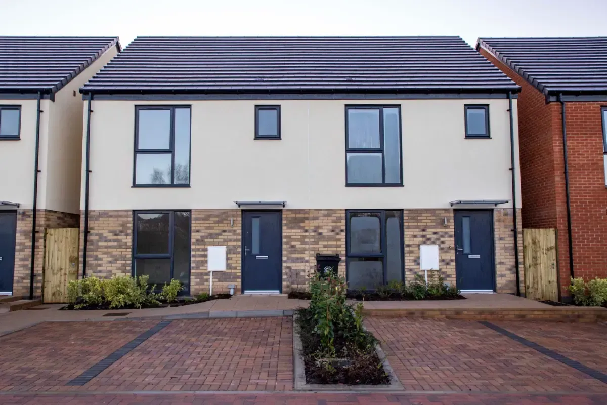 Modern semi-detached townhouse with blue doors and brick driveway, seen from the front