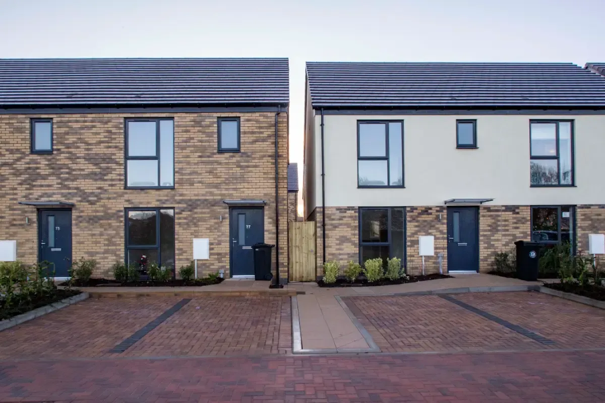 Modern brick townhouses with dark doors and windows, fronted by a paved driveway and small shrubs