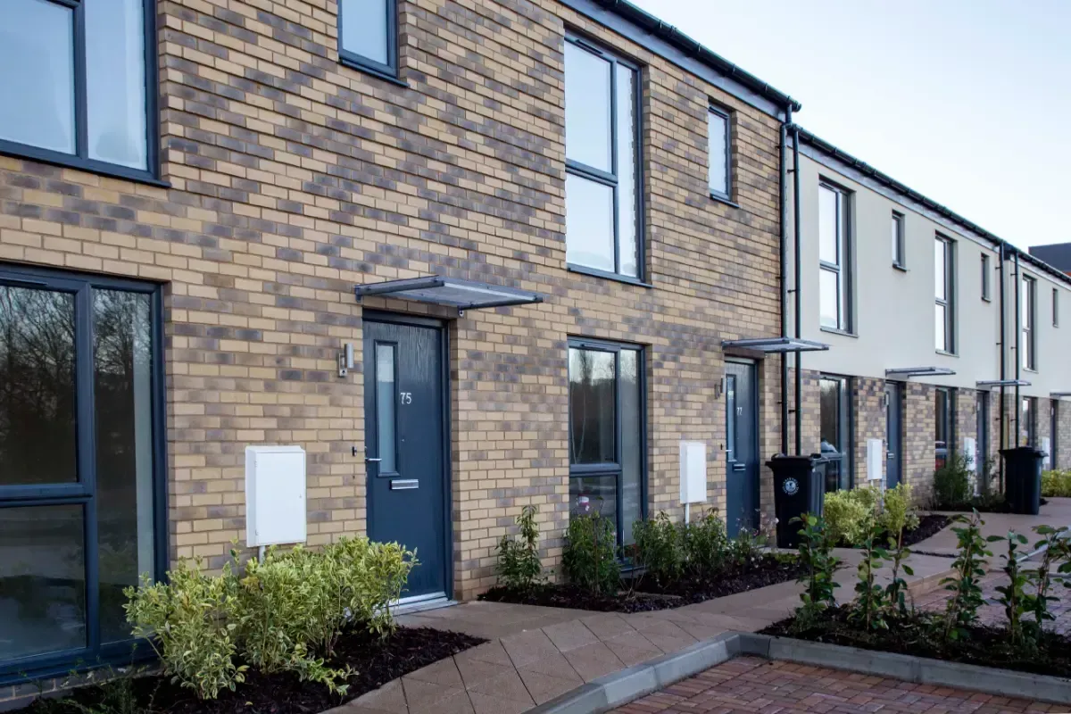 Row of modern brick townhouses with front doors and small landscaped gardens.