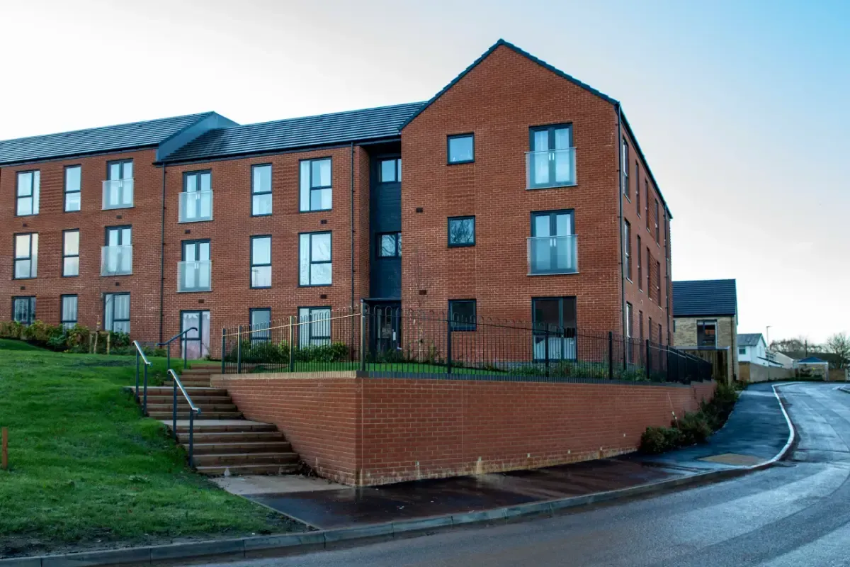 Red brick apartment building beside a curved road, with a grassy slope and stairs in front