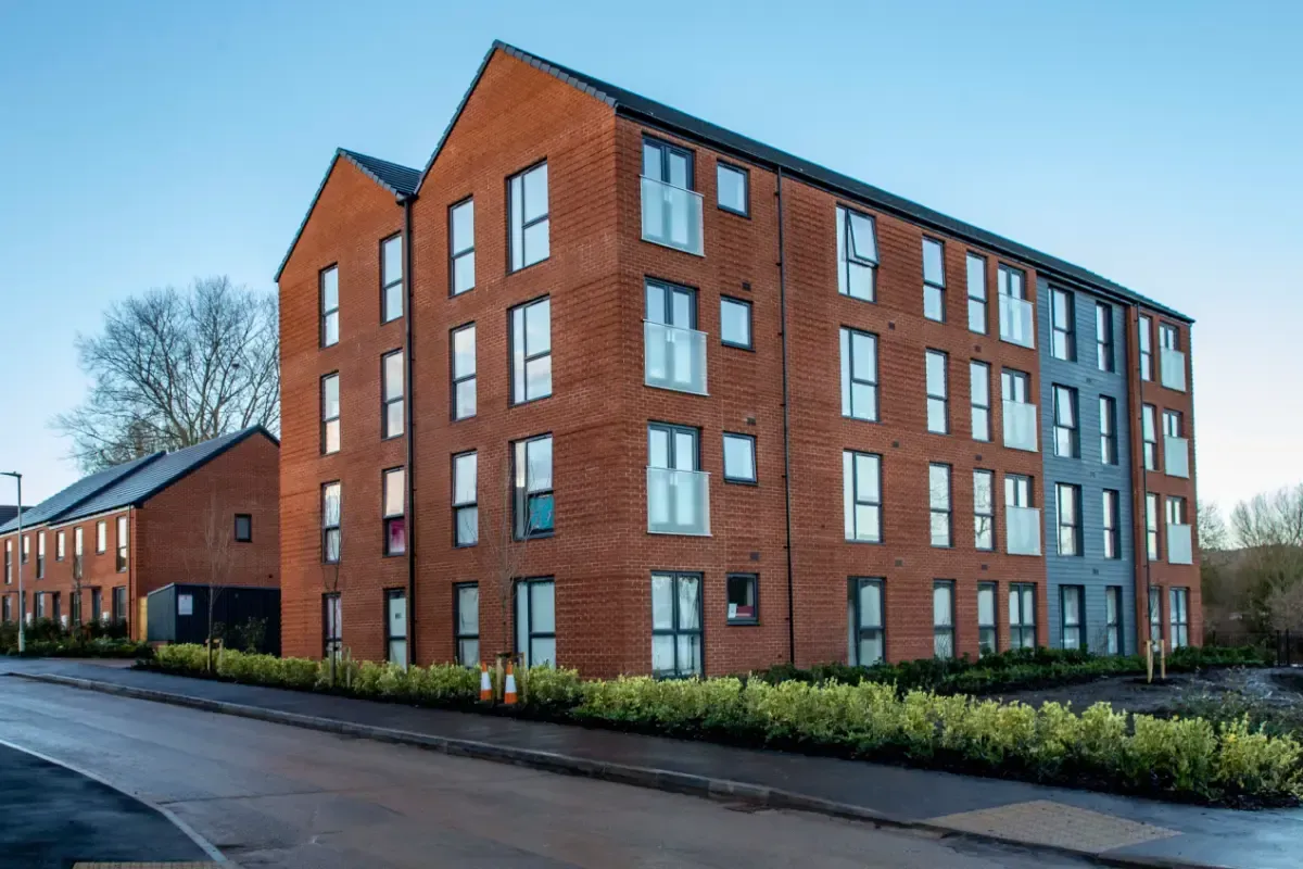 Red brick apartment building with many windows beside a wet road on a cloudy day