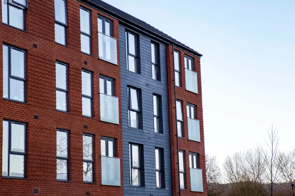 Modern apartment building with red brick, dark gray panels, and tall white-framed windows against a blue sky