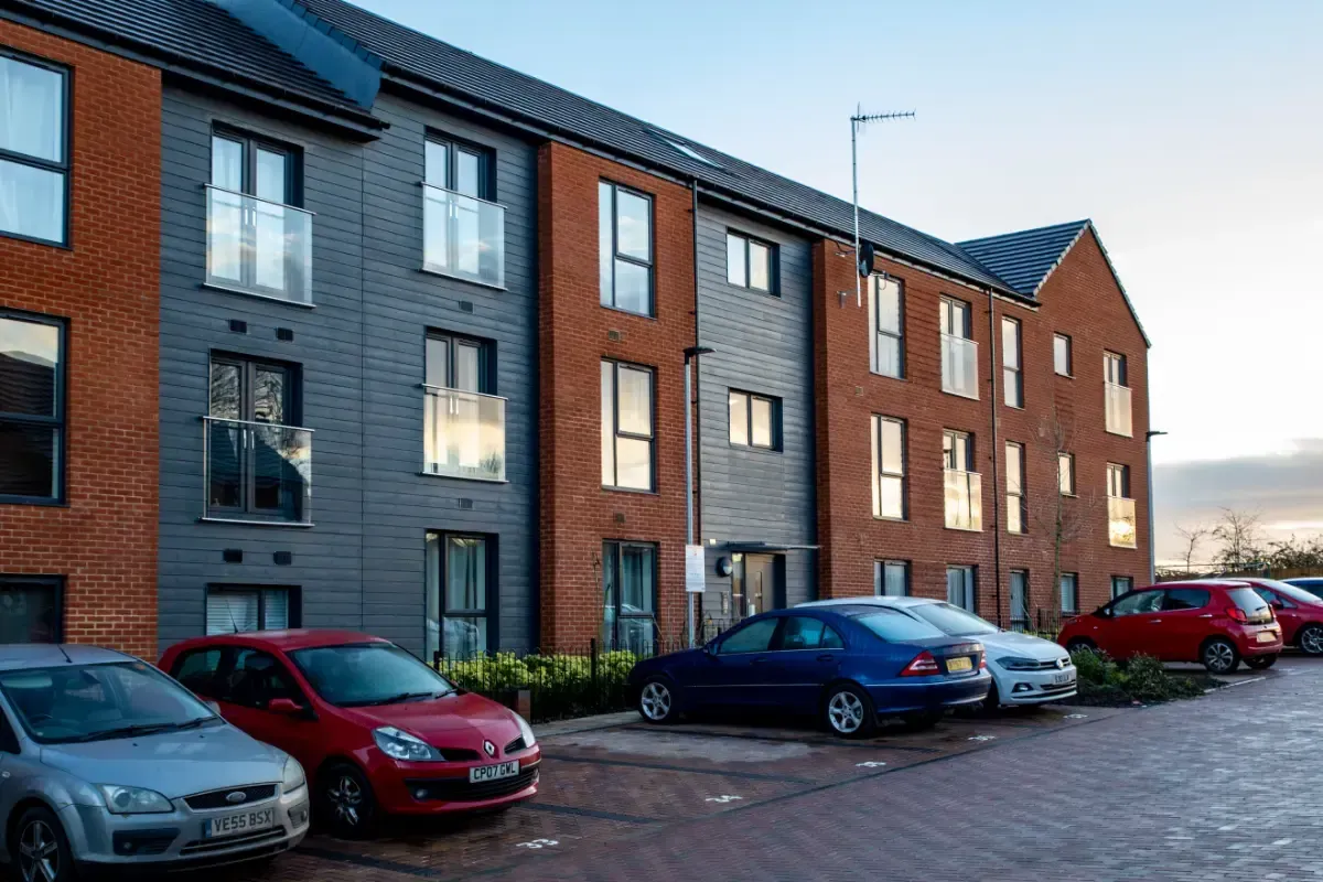 Modern apartment building with parked cars along a cobblestone street at dusk