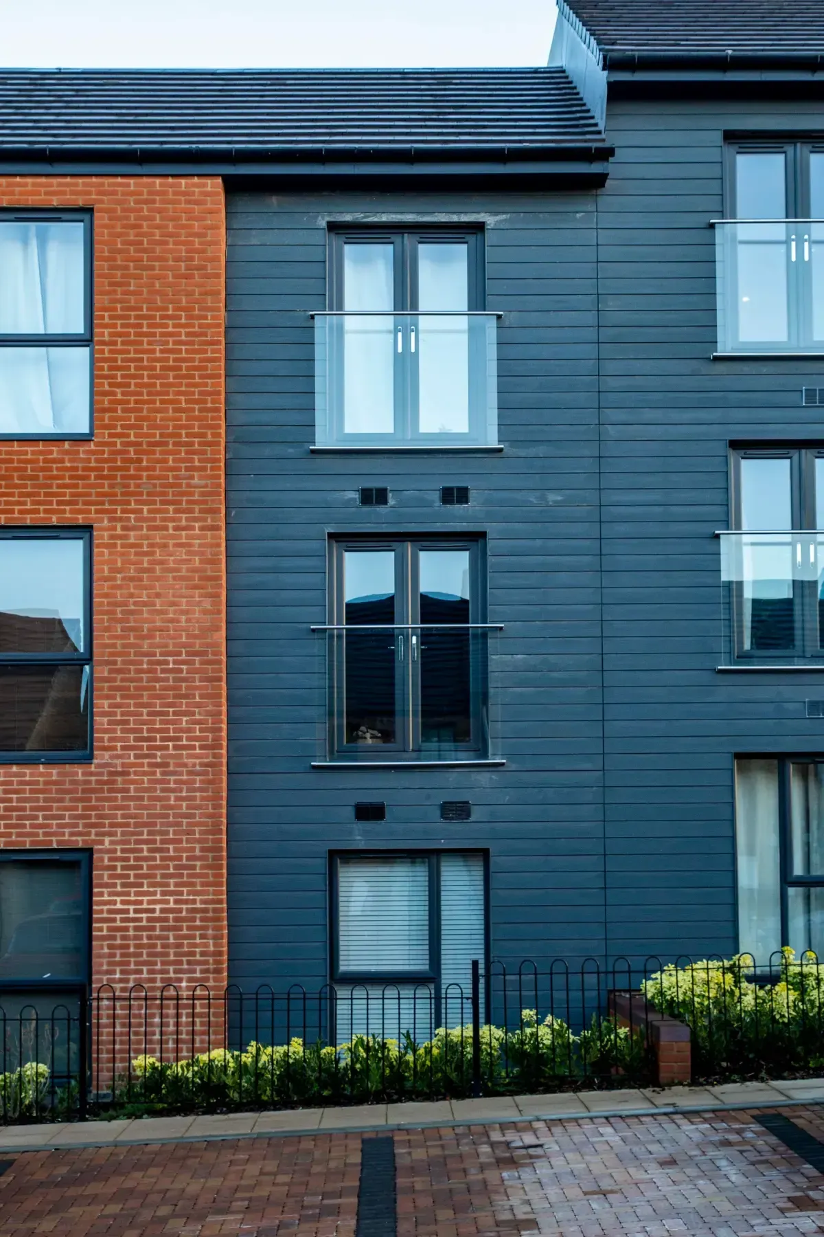Modern townhouse facade with blue siding, brick side wall, and windows above a paved walkway