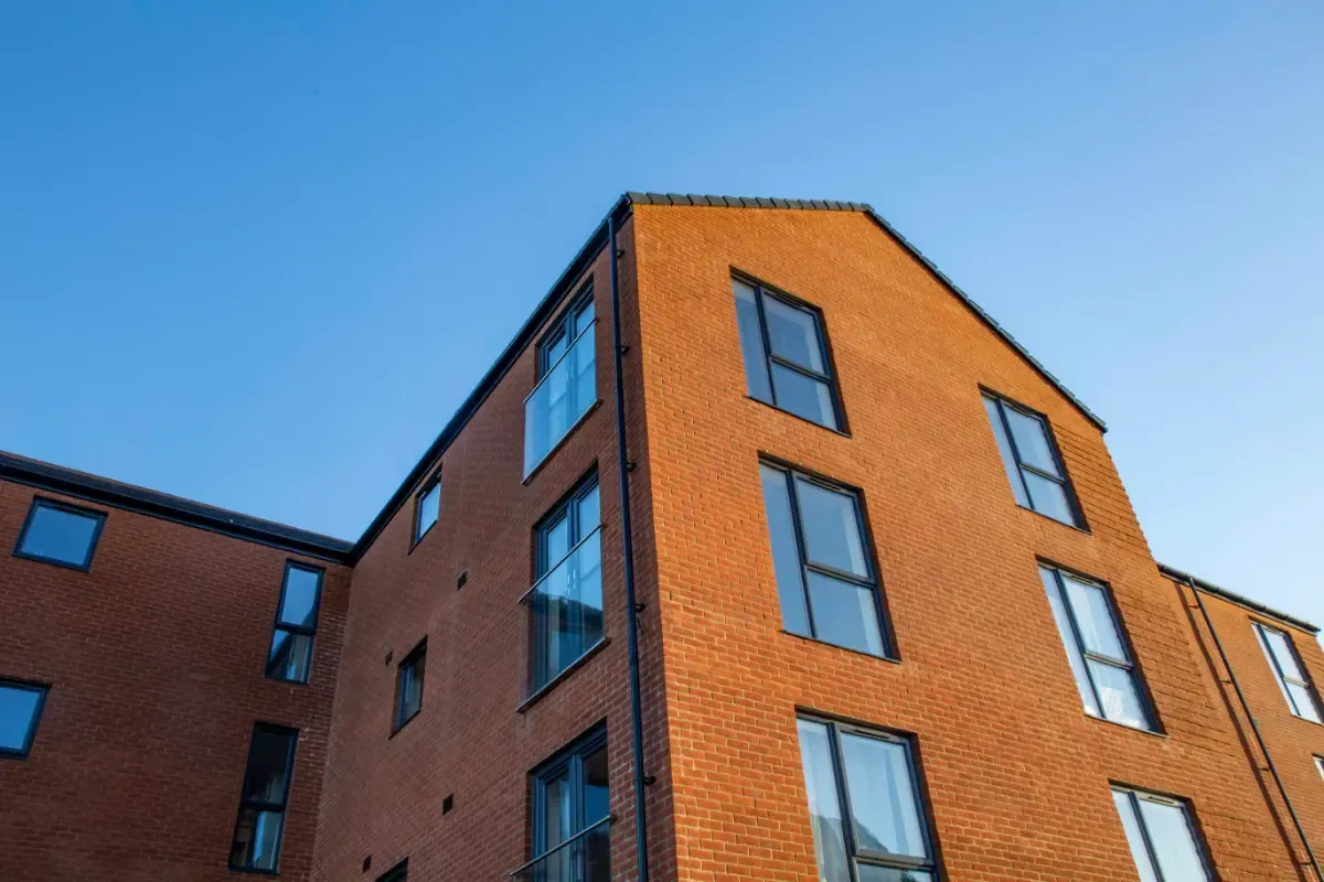 Red brick apartment building viewed from below against a blue sky