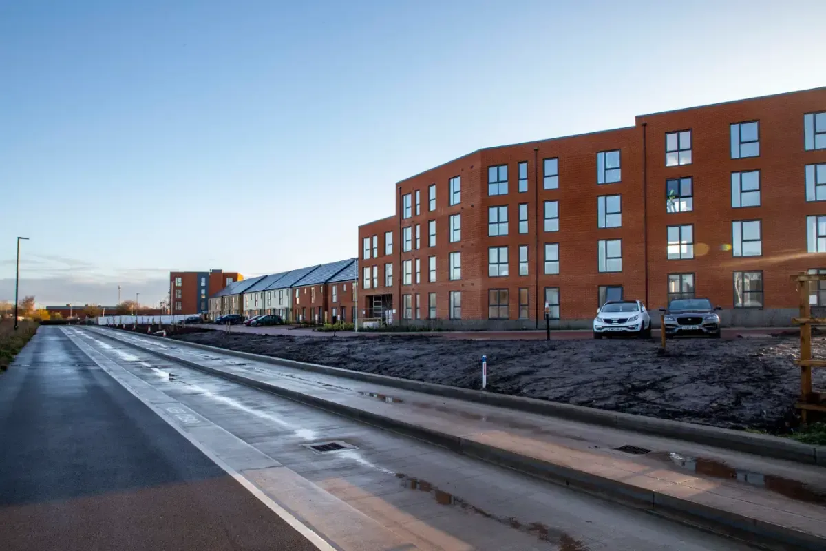 Row of red brick apartment buildings beside a wet road under a clear sky