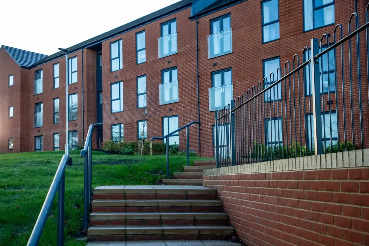 Red-brick apartment building with stairs, handrails, and grassy hillside entrance