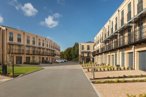 Modern apartment courtyard with beige townhouses, balconies, and a paved driveway under a blue sky