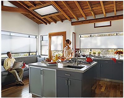 Love is Blinds: A man is reading a newspaper while a woman prepares food in a kitchen, roller shades on windows.