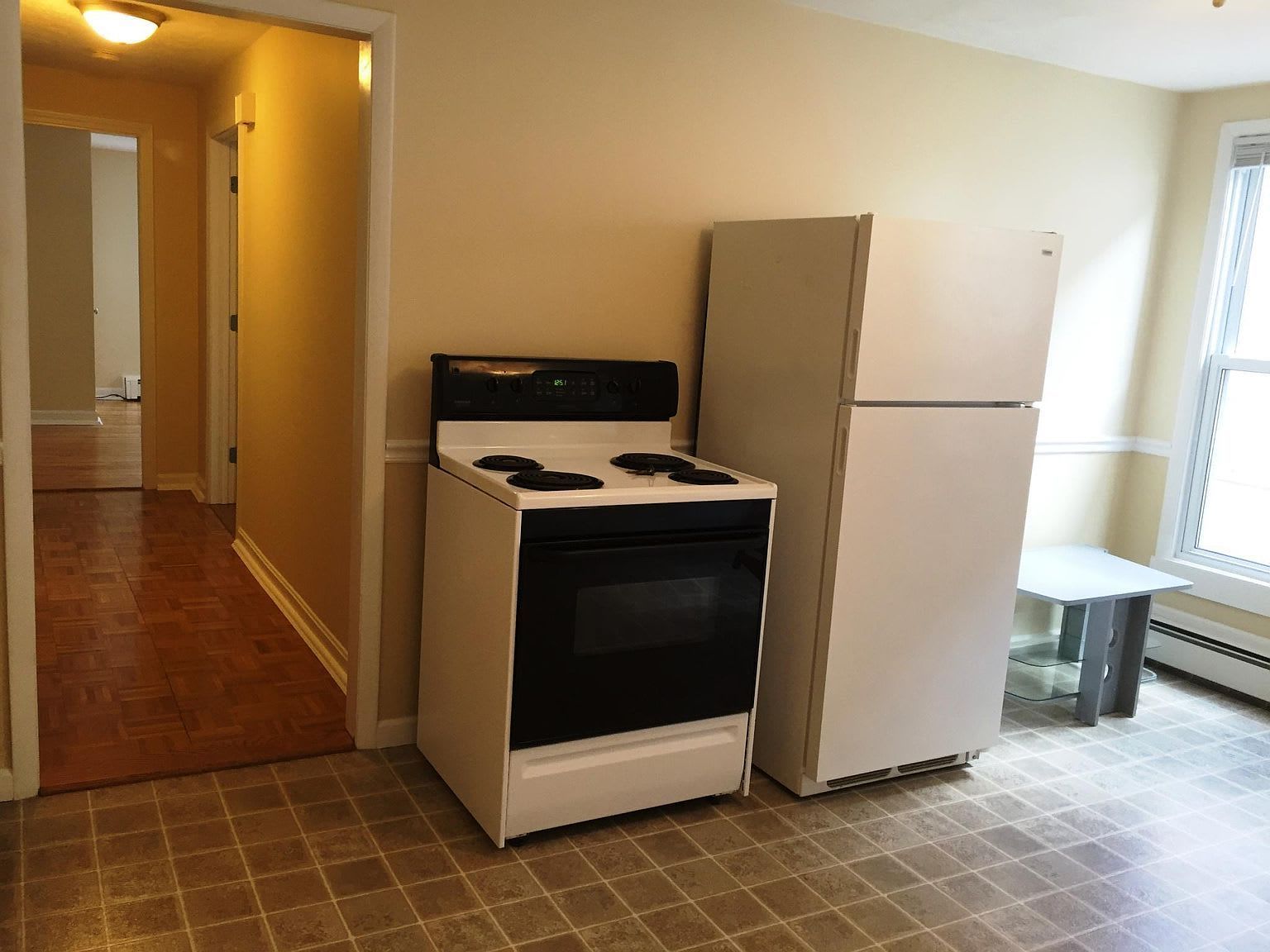 Kitchen with a stove, refrigerator, and doorway leading to a hallway with wood flooring.