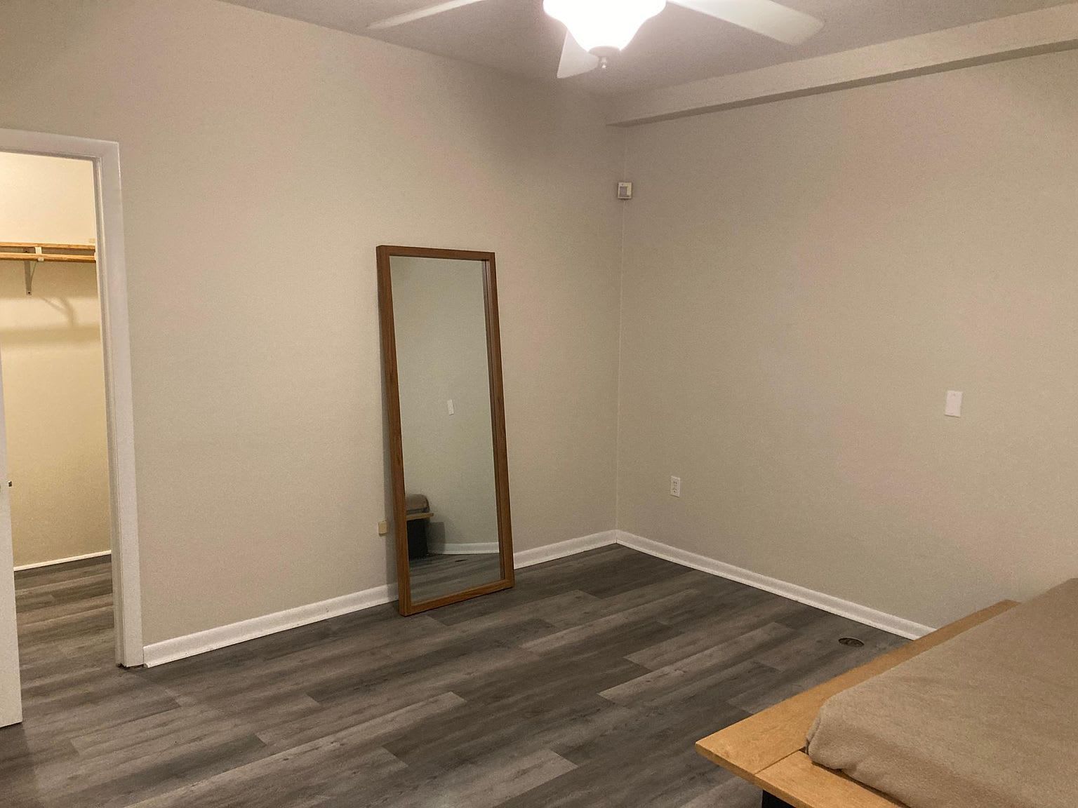 Empty bedroom with wood-look flooring, large mirror, and partial view of a bed.