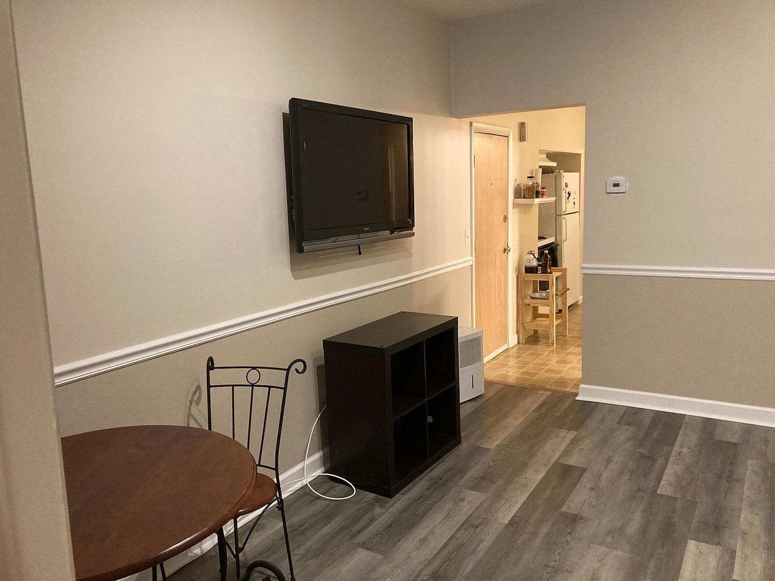A small living space with a mounted TV, dark brown storage unit, and round table.