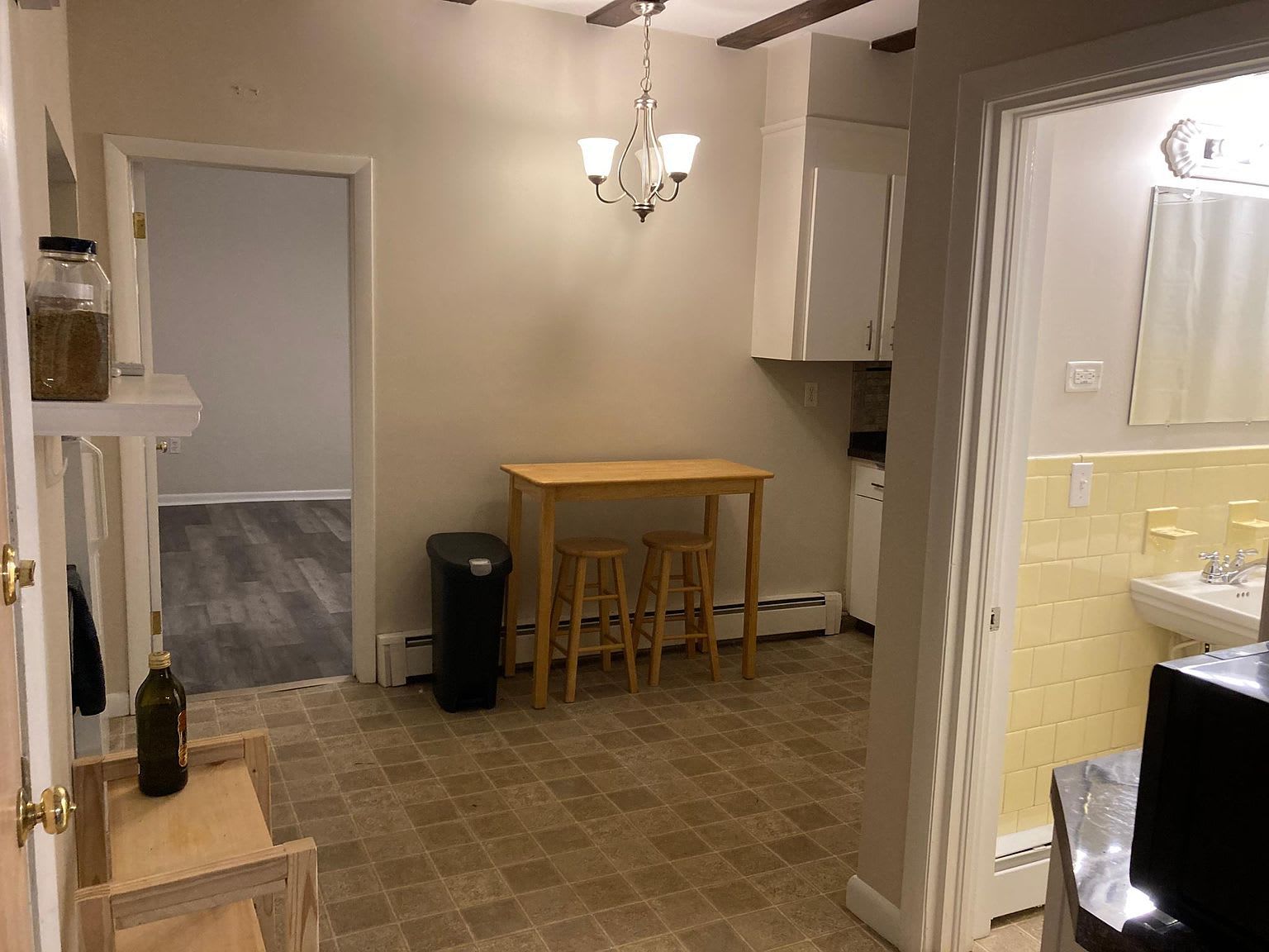 Kitchen with table, stools, and open doorway to another room. Yellow-tiled bathroom visible.