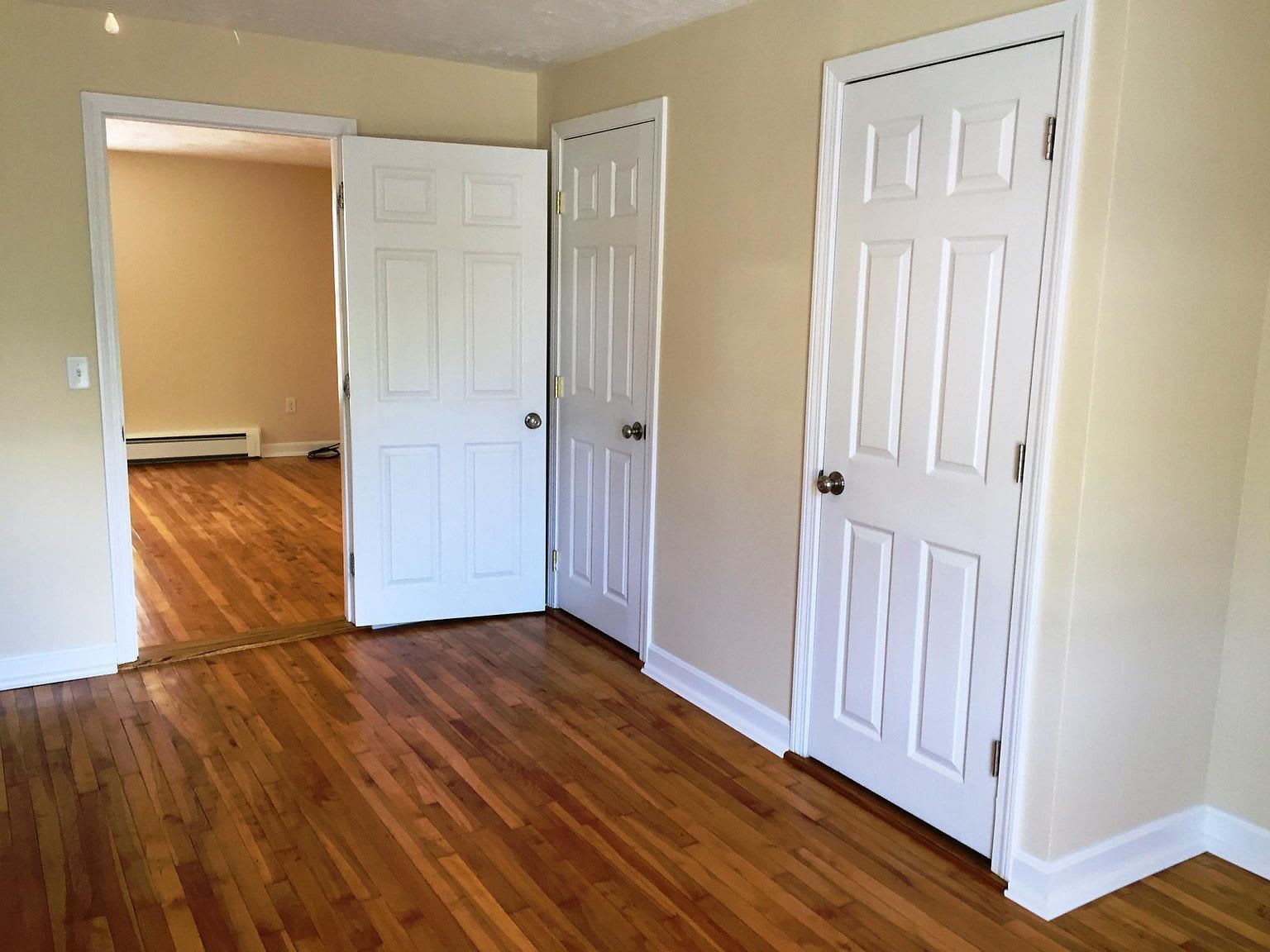 Empty room with hardwood floors, three white doors, and a doorway to another room.
